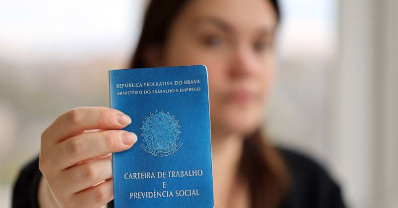 Mulher em primeiro plano desfocada segurando e mostrando a Carteira de Trabalho em foco principal para planejamento de crédito